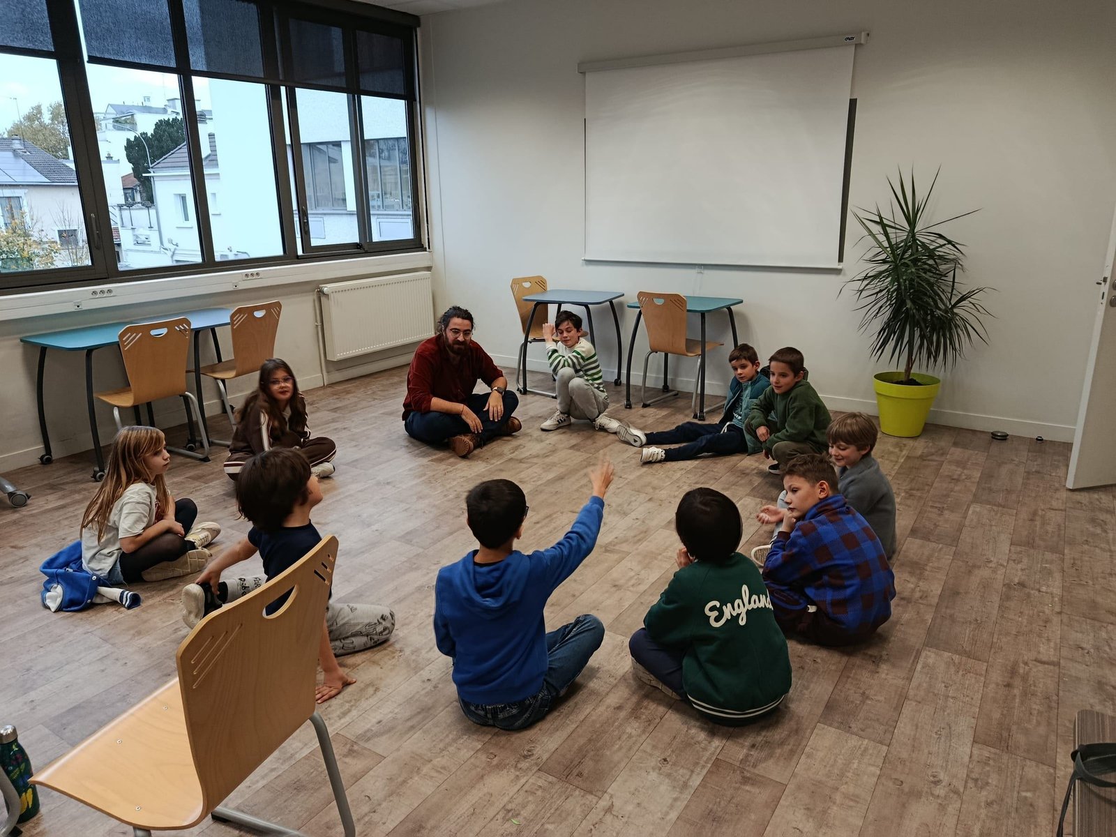 Le cercle du début : Yannis et les enfants assis au sol, une main se lève