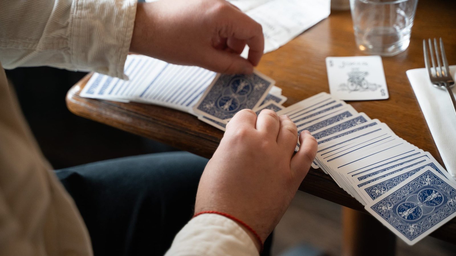 Les mains d'un élève au-dessus d'un jeu de cartes étalé sur une table de café, guidées par la main du magicien